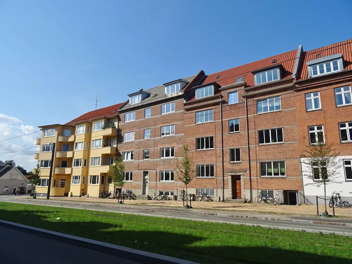 Etageejendomme i gul og rød mursten langs en grøn vejkant